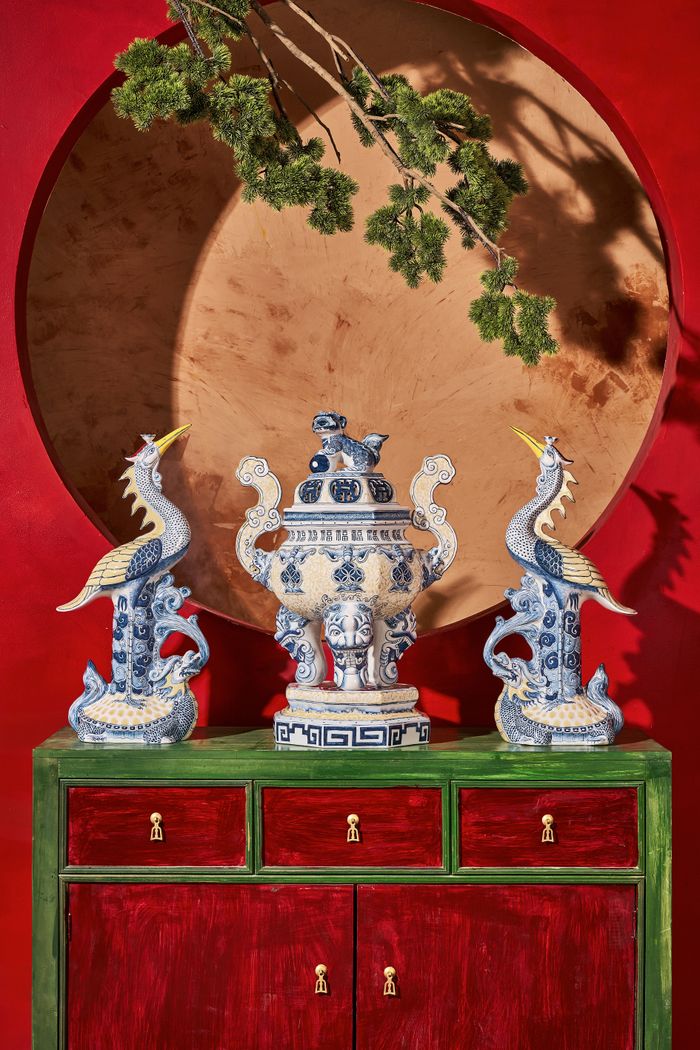 Ornate vase and blue figurines on a red cabinet with a circular backdrop, exuding a classic artistic style.