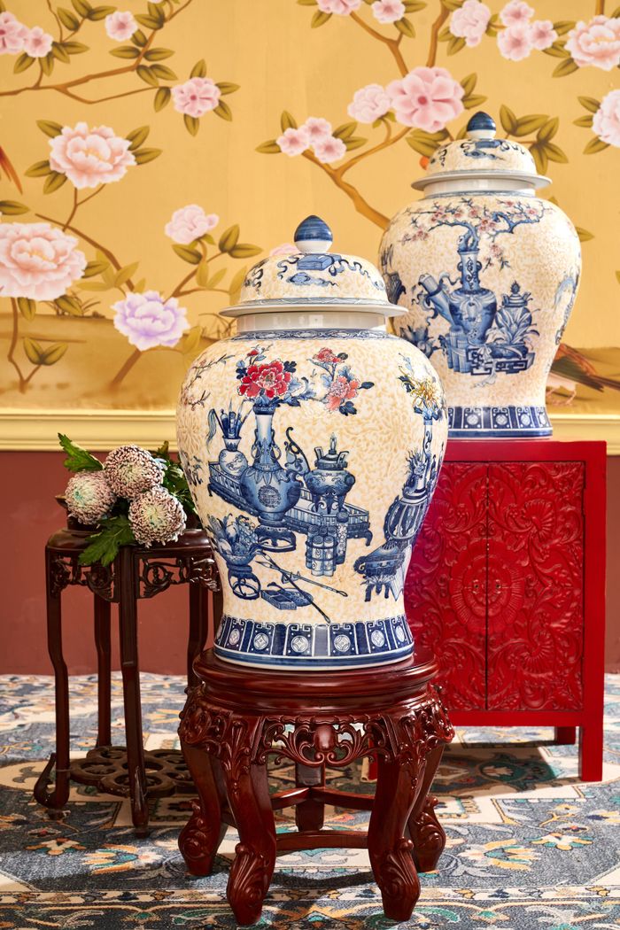Decorative porcelain vases on wooden stands with floral wallpaper background.