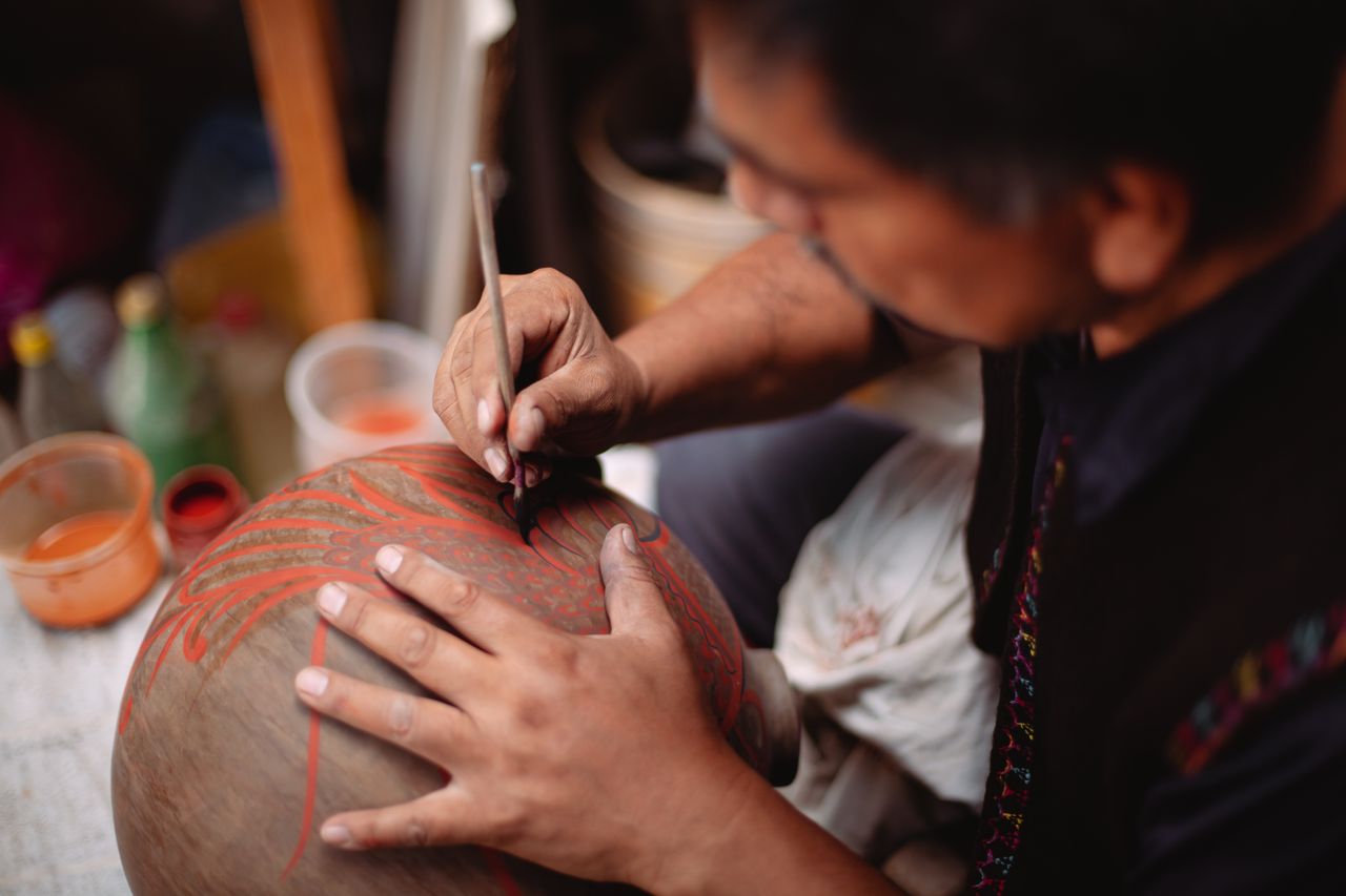 About A focused artisan carefully painting intricate designs on a clay pot, showcasing craftsmanship.